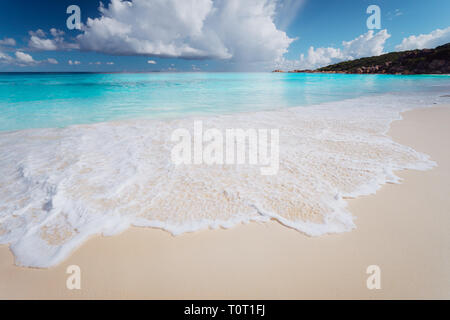 Les couleurs de l'eau incroyable de Grande Anse, l'île de La Digue aux Seychelles. Écume de mer sur la plage tropicale avec d'imposants nuages blancs. Locations de contexte Banque D'Images