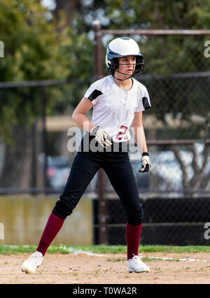 L'adolescence féminine de softball player en noir et blanc en uniforme un prudent mènent à partir de la première base. Banque D'Images
