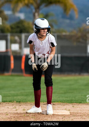 L'adolescence féminine de softball player en uniforme noir et blanc montrant de grands yeux à l'intérieur de son casque tandis que sur la deuxième base. Banque D'Images