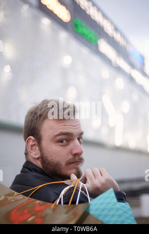 Un jeune homme, 29 ans, shopping sur son dos, à dos à la caméra. l'extérieur en face d'un centre commercial. Banque D'Images