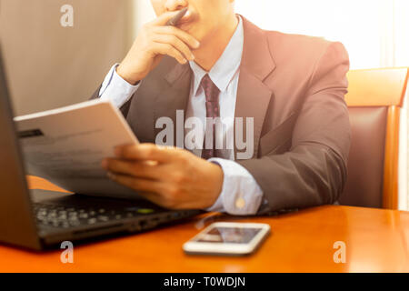 Businessman reading paperwork formulaire avec un ordinateur portable sur un bureau en bois. Banque D'Images