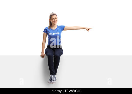 Portrait d'un bénévole féminin assis sur un panneau blanc et pointant dans une direction isolé sur fond blanc Banque D'Images