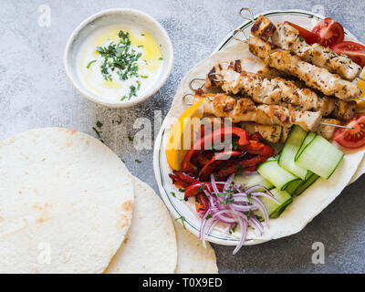 Brochettes de poulet grillé sur le métal avec des légumes frais sur le pain pita grec et sauce dans un bol sur un fond gris. La cuisine grecque. Banque D'Images