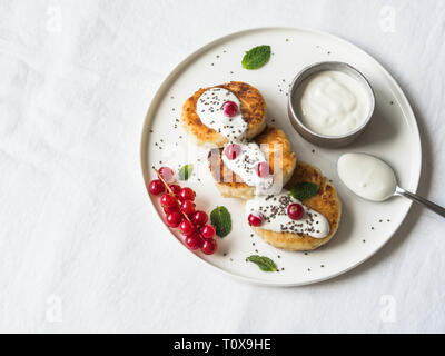Gâteaux de fromage maison fromage blanc servi sur une plaque en céramique blanche à la menthe, la crème sure et de groseille rouge sur un fond blanc. Banque D'Images