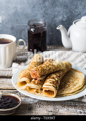 Fédération des crêpes levures roulé dans un tube sur plaque blanche, de la confiture et du thé dans la tasse sur la table. Crêpes de blé traditionnelles pour le Mardi Gras. Banque D'Images