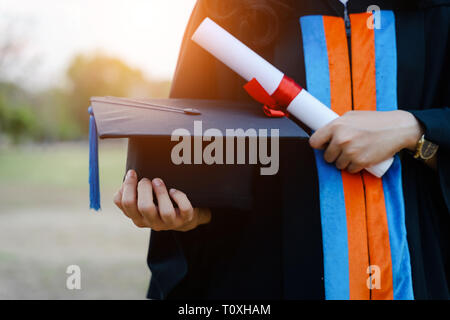 Les diplômés de l'université, très souriants, portent une robe de graduation noire et un stand de chapeau à l'extérieur du hall après avoir reçu un diplôme en début de diplôme Banque D'Images