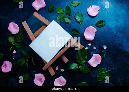 Chevalet d'artiste avec des pétales de rose et de feuilles sur un fond humide avec l'exemplaire de l'espace. Modèle vierge pour une peinture aquarelle Banque D'Images