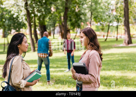 Selective focus of girls talking while standing avec livres près de étudiants au football Banque D'Images