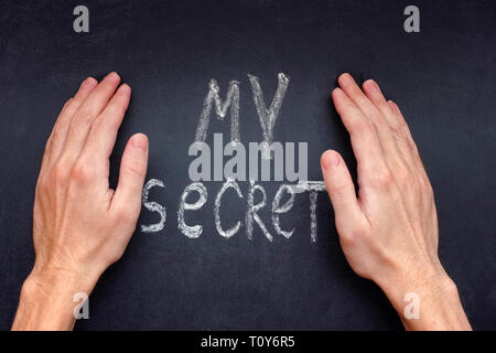 Mains couvrant jusqu'mots mon secret sur un tableau. Banque D'Images