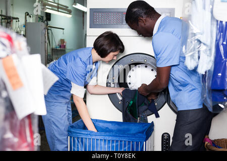 Les travailleurs qualifiés de blanchisserie avec son collègue masculin africain loading lave-linge avec les vêtements sales Banque D'Images
