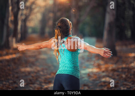 Femme exerçant à l'extérieur, dans un parc public. Debout avec les bras levés. Banque D'Images