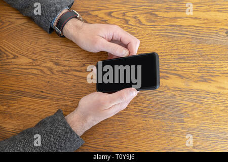Homme tenant un téléphone intelligent dans les mains en attendant d'être servis au restaurant. Téléphone avec écran incurvé noir vide Banque D'Images