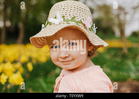 Cute blonde little girl smiling avec jonquilles jaune au printemps. Banque D'Images