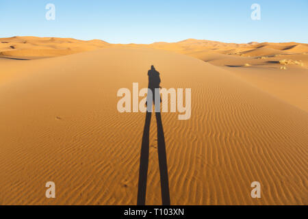 La fin de l'article faible soleil projette une ombre humaine sur les imposantes dunes de sable de l'Erg Chebbi, Maroc, offre une vue splendide de courbes et de formes et de l'évolution Banque D'Images