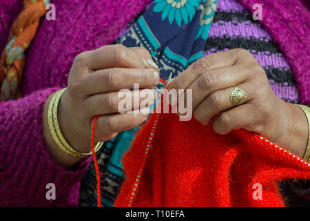 Les mains de tricot. Faire un vêtement de laine teints à partir de la laine des moutons. Femme portant un pull en laine tricoté cardigan et haut. Le tricot en s'en allant au marché. Himalayan Foothill village, nord de l'Inde. Banque D'Images