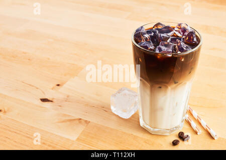 Café glacé ou latte macchiato dans grand verre avec paille sur table en bois. L'espace de copie pour le texte. Banque D'Images