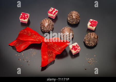 Chocolat pralines de luxe décorées dans des tons rouges attachés arc. Cadeau Anniversaire Mariage engagement Saint-valentin Pâques fête événement et concept. Banque D'Images