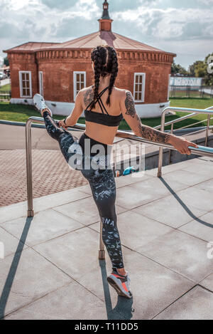 Gymnaste fille se tient un des groupes, en été, la formation de la ville des muscles des jambes, athlète, la peau tannée des tatouages. Chauffe les muscles, avant la formation de la ville d'été Banque D'Images