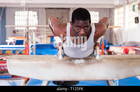 L'homme afro adultes sportswear en faisant des exercices sur appareils de gymnastique acrobatique dans hall Banque D'Images