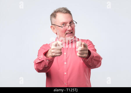 Man excité en chemise rouge portant des lunettes caméra pointer du doigt et isolé sur un fond blanc. Il est convenu avec vous et heureux avec votre ch Banque D'Images