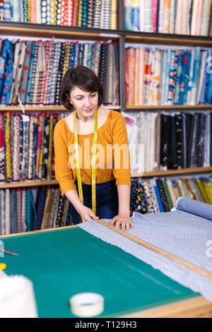 Vendeuse compétente a ordonné de mesure pour la coupe de tissu textile en boutique, la préparation pour la vente Banque D'Images