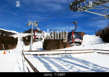 Jasna, Slovaquie - 22 janvier 2019 : les cabines du téléphérique à la station et vue sur les pistes du côté sud de la montagne Chopok dans un ciel ensoleillé Banque D'Images