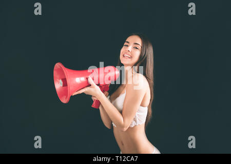 Jeune femme criant avec un mégaphone. Jeune femme avec de longs cheveux noirs est isolé sur fond noir. La jeune fille a une figure du sport, il est tr Banque D'Images