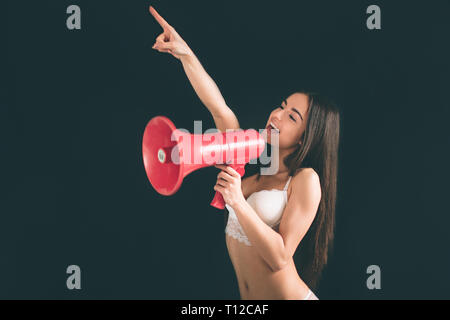 Jeune femme criant avec un mégaphone. Jeune femme avec de longs cheveux noirs est isolé sur fond noir. La jeune fille a une figure du sport, il est tr Banque D'Images