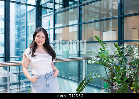 Un jeune étudiant asiatique se trouve dans un bâtiment moderne en verre, où elle étudie, Banque D'Images