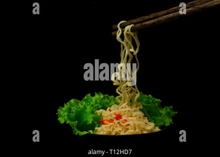 Bol de nouilles avec légumes isolé sur noir, nouilles chinoises séchées avec du porc frit croustillant faire léviter dans les airs isolé sur fond noir. Banque D'Images