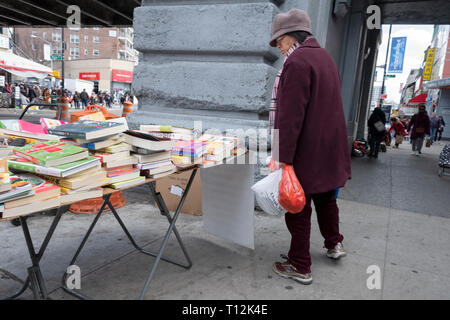 Une femme asiatique chinois inspecte les livres en vente sur un stand sur la rue Main sous le LIRR pistes. Dans le quartier chinois, le rinçage, Queens, New York. Banque D'Images