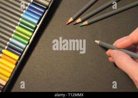 Une photographie d'un ensemble de crayons de couleur, 3 sur du papier noir sur prêt, avec une main tenant une coloration blanc crayon et copie espace pour ajouter du texte Banque D'Images