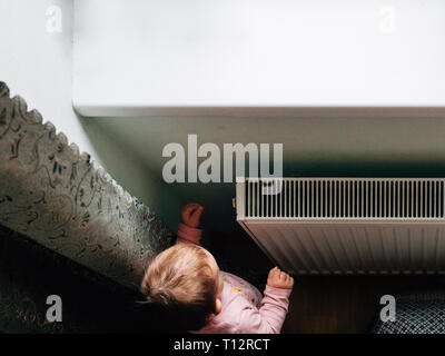 Portrait d'un adorable bébé près du radiateur à la maison Banque D'Images