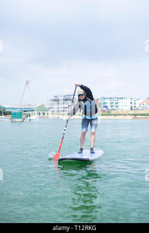 Un mâle en stand up paddle boarder à Hove Lagoon Banque D'Images