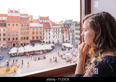 Jeune femme assise à l'extérieur par l'intermédiaire de rebord de fenêtre de l'appartement avec vue sur la place du vieux marché de la ville de Varsovie, Pologne rêver Banque D'Images