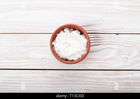 L'huile de noix de coco dans un bol d'argile brun sur table de cuisine en bois blanc Banque D'Images