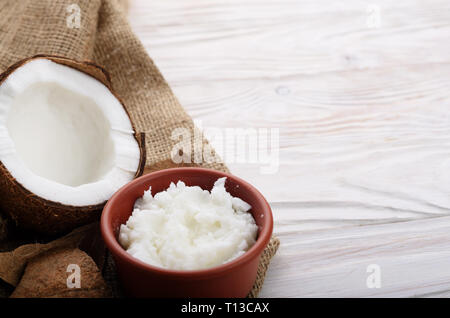 L'huile de noix de coco dans un bol d'argile brun et shell avec de la viande sur le chanvre sacs sur une table de cuisine en bois blanc Banque D'Images