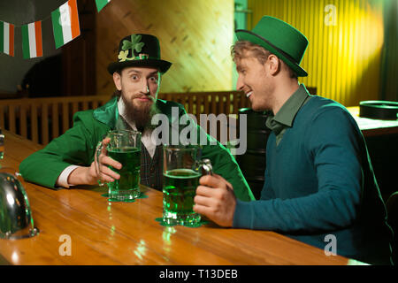 Dark-haired jeune homme barbu dans un lutin hat et son ami ont beaucoup de temps dans le pub Banque D'Images