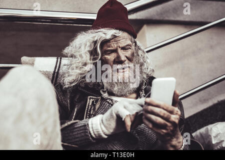 Vieil homme à regarder sans-abri comme sur les photos de sa famille sur l'écran. Banque D'Images