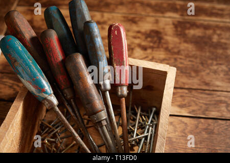Jeu de tournevis old vintage usé avec poignées en bois debout dans une caisse en bois avec différents équipages dans le bas sur une table rustique Banque D'Images