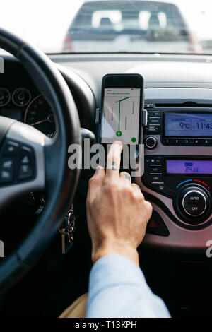 Close-up de l'homme avec l'aide de voiture conduite main tatouée téléphone cellulaire comme système de navigation Banque D'Images