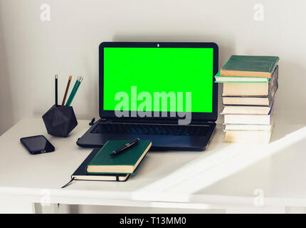 Ordinateur portable écran vert, pile de livres, crayons et bloc-notes sur le tableau blanc, de l'éducation office concept background Banque D'Images