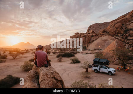 La Namibie, Spitzkoppe, amis assis sur un rocher à regarder le coucher du soleil Banque D'Images
