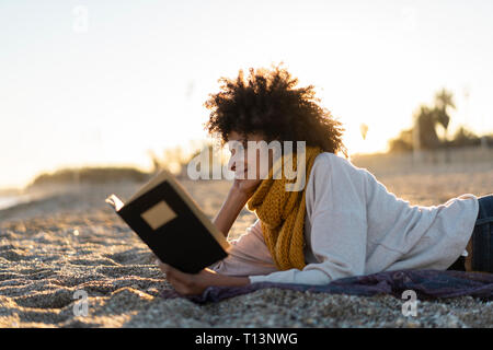 Femme couchée dans le sable, se détendre sur la plage, la lecture d'un livre Banque D'Images