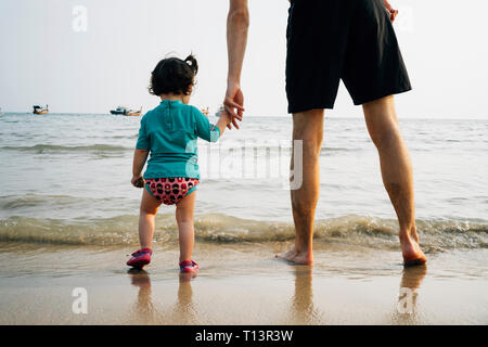 La Thaïlande, Koh Lanta, vue arrière de baby girl wearing UV protection shirt debout avec son père à bord de mer Banque D'Images
