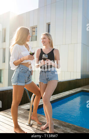 Copines sur une terrasse sur le toit, s'amuser à la piscine, boire du vin rouge Banque D'Images