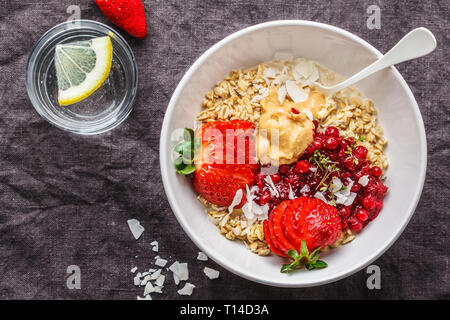 Porridge aux fruits rouges, le beurre d'arachide et noix de coco dans un bol blanc. La nourriture végétalienne saine concept. Banque D'Images