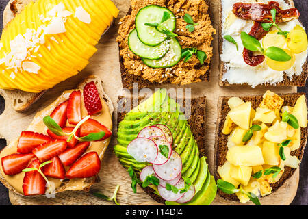 Différents types de sandwichs à la mangue, fraise, tofu pate, avocat, pommes de terre et de la ricotta sur un fond sombre. Banque D'Images