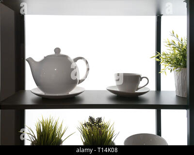 Plateau rétroéclairé avec fragment ustensiles de silhouettes. théière électrique de plantes en pot sur l'étagère en bois mur blanc fond cuisine Banque D'Images