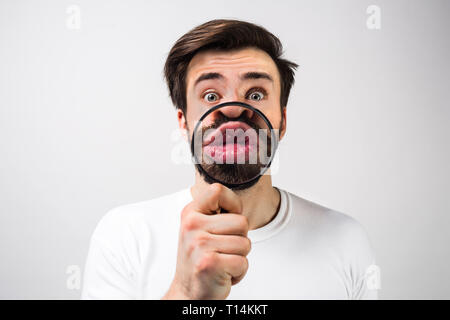 L'homme étrange et étonné isolé sur fond blanc et de faire de l'amusement avec mettre une loupe devant sa bouche. Guy a l'air tout à fait inhabituel de cette Banque D'Images